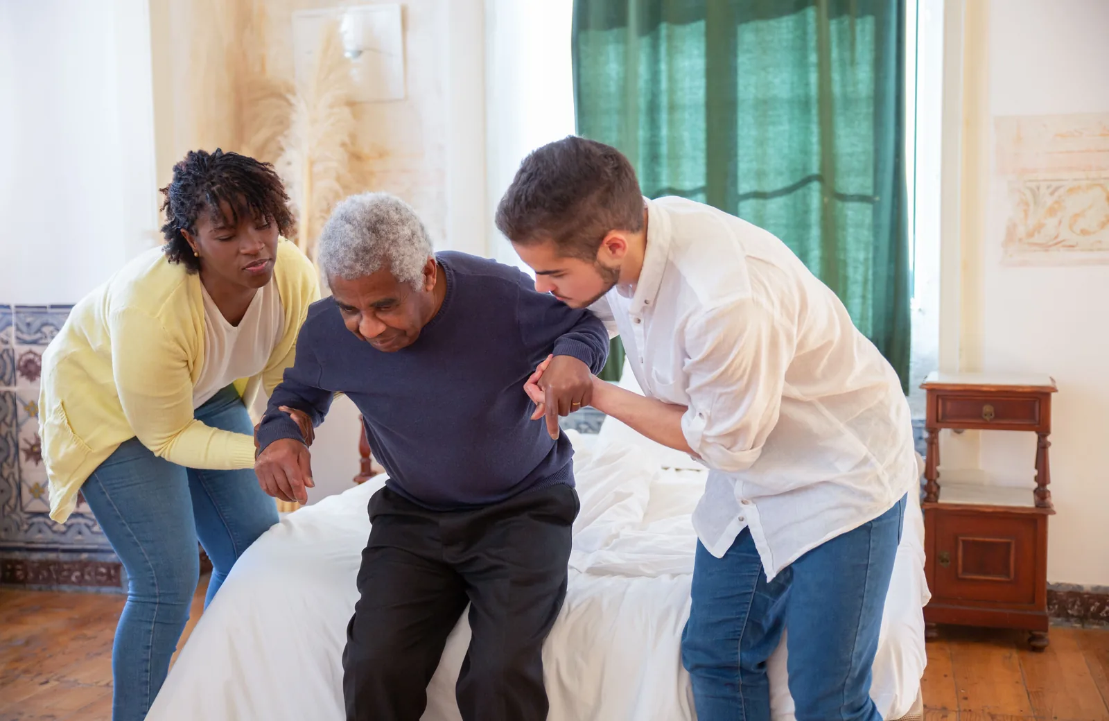 Two support workers helping an older man to his feet